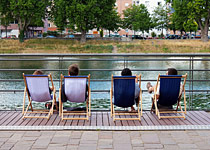 Gruppe von Menschen sitzt auf Liegestühlen und schaut aufs Wasser